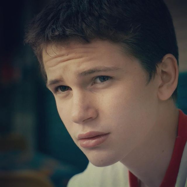 Gabriel Bateman looking left with a white V-neck T-shirt with red borders